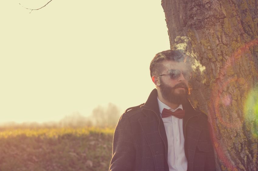 Sad hipster guy smokes outdoors in field
