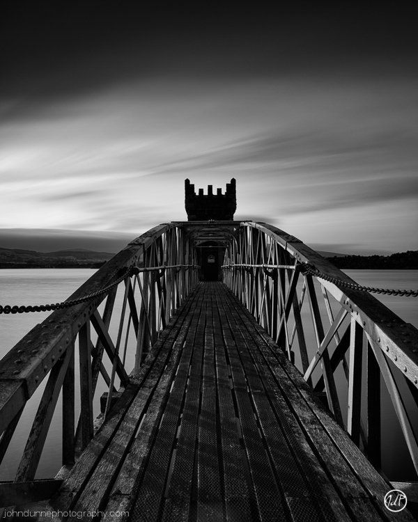 The Sun begins to set, casting its soft light upon the 1900's tower and bridge at Vartry Reservoir in Wicklow, Ireland as dark ominious storm clouds move in overhead