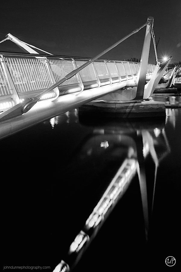 Standing at night at the edge of the IFSC, Dublin cable pedestrian bridge looking back across the river Liffey with the bridge of the left.
