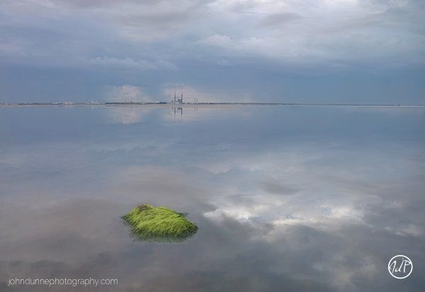 A tranquil image taken just after a thunderstorm where the clouds are perfectly mirrored in the calmness of Dublin bay, with the chimney stacks of Poolbeg Generating Station in the background.
