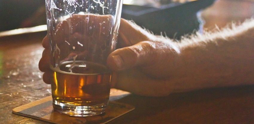 Close up of a man's hand grasping a mostly drunk, glass of beer with trails of suds on a bar coaster