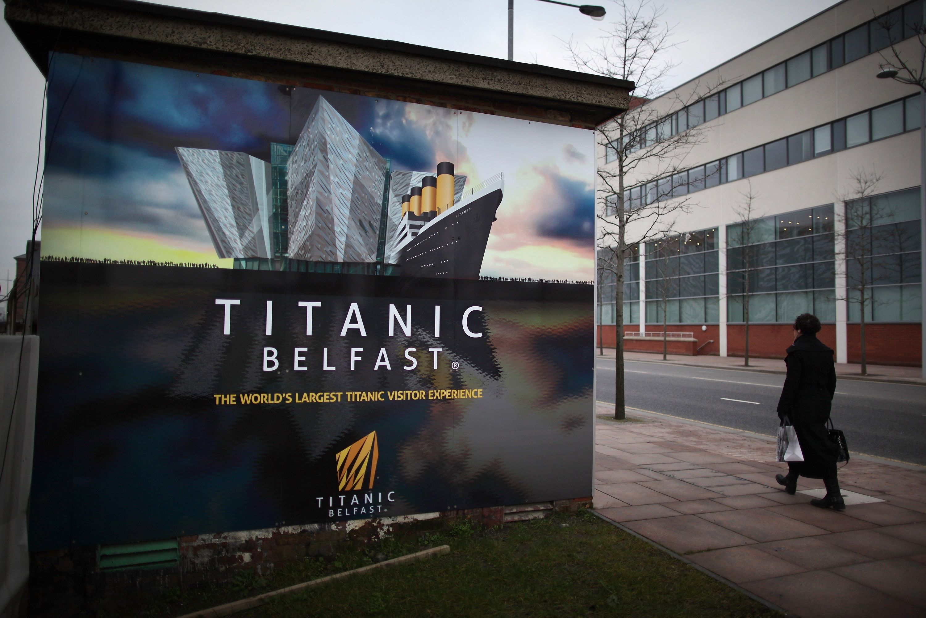 BELFAST, NORTHERN IRELAND - MARCH 13: A woman walks past a hoarding advertising the Titanic Belfast attraction in The Titanic Quarter on March 13, 2012 in Belfast, Northern Ireland. Belfast's Titanic Quarter is a regeneration area on the original site of the Harland and Wolff shipyard - birthplace of RMS Titanic. The Titanic Belfast Experience is a new £90 million visitor attraction which opens on March 31, 2012. The ill-fated passenger liner sank after hitting an iceberg in the Atlantic on the night of April 15, 1912 with the loss of 1517 lives. (Photo by Peter Macdiarmid/Getty Images)