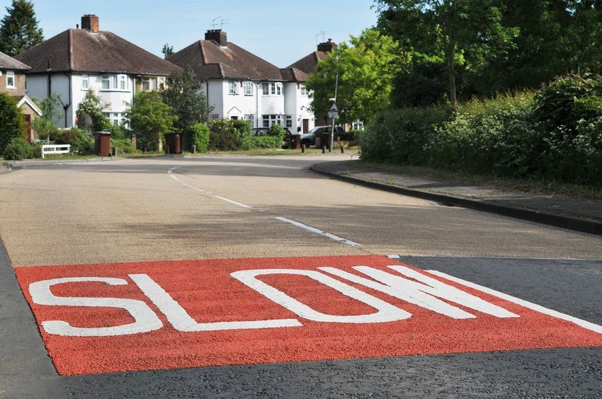 "SLOW" in white on a red background painted onto a quiet residential English road.
