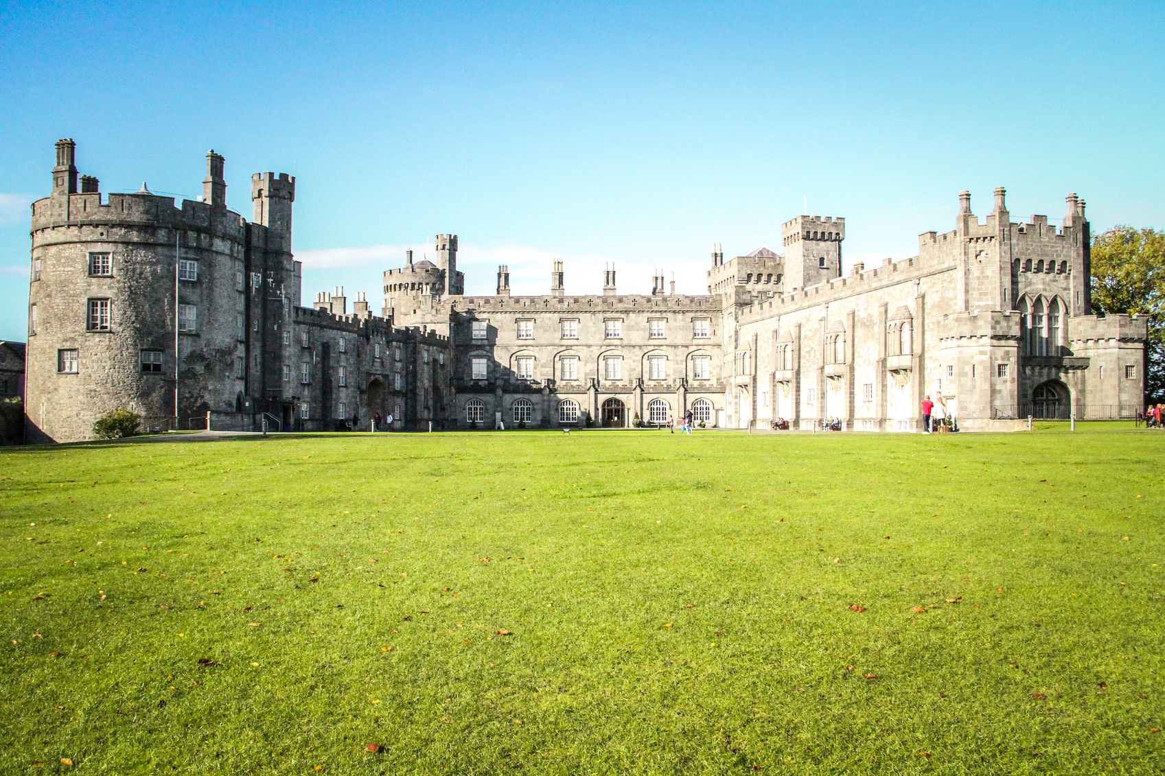 Kilkenny, Ireland - October 31, 2013 : People are walking around a main tourist attraction in Ireland, the Kilkenny Castle. On the right a man with a red top is taking a picture.