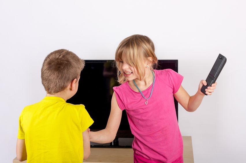 Siblings arguing over the remote control in front of the television.